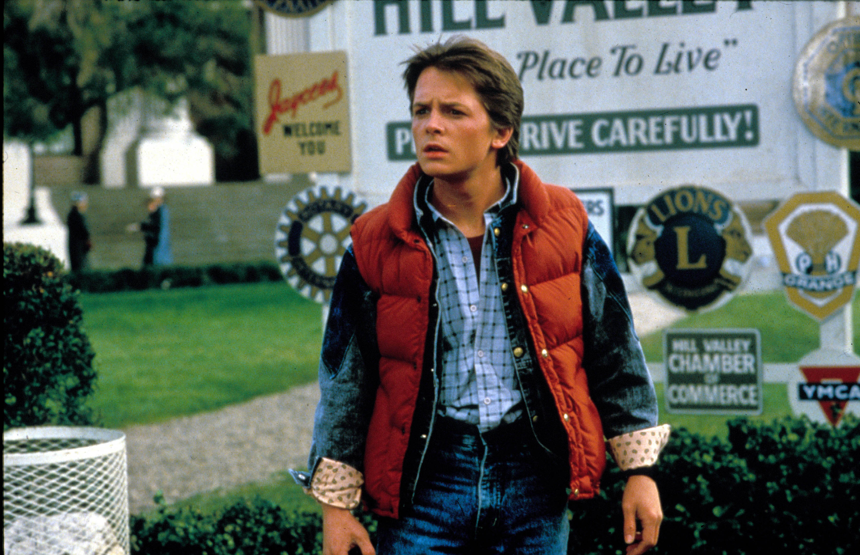 Michael J. Fox stands in a puffy jacket and all-denim wardrobe, staring at something confusing near a park