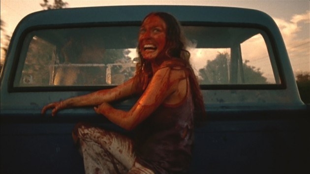 A distraught woman covered in blood sits in a truck bed
