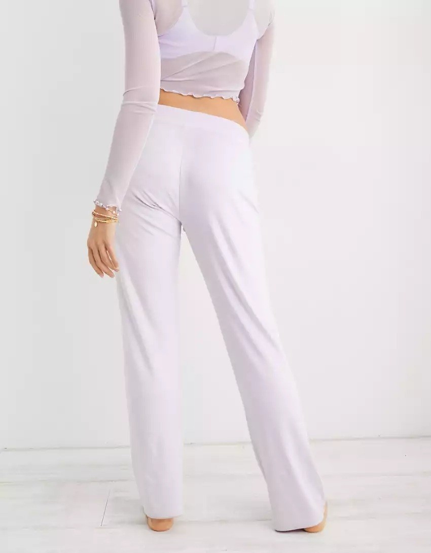 A back shot of the model from the neck down wearing the pants in lavender with a matching mesh top