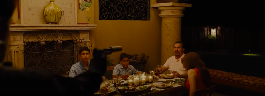 A man aims a gun at a family eating dinner around their table