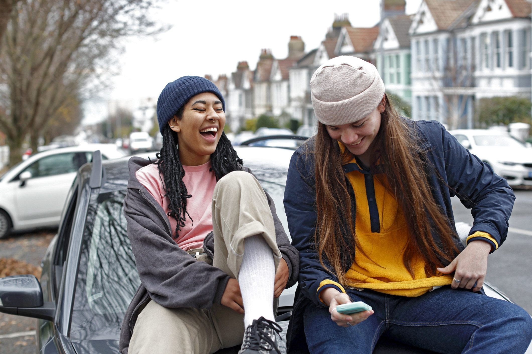 Two teens sitting on the hood of a car and laughing