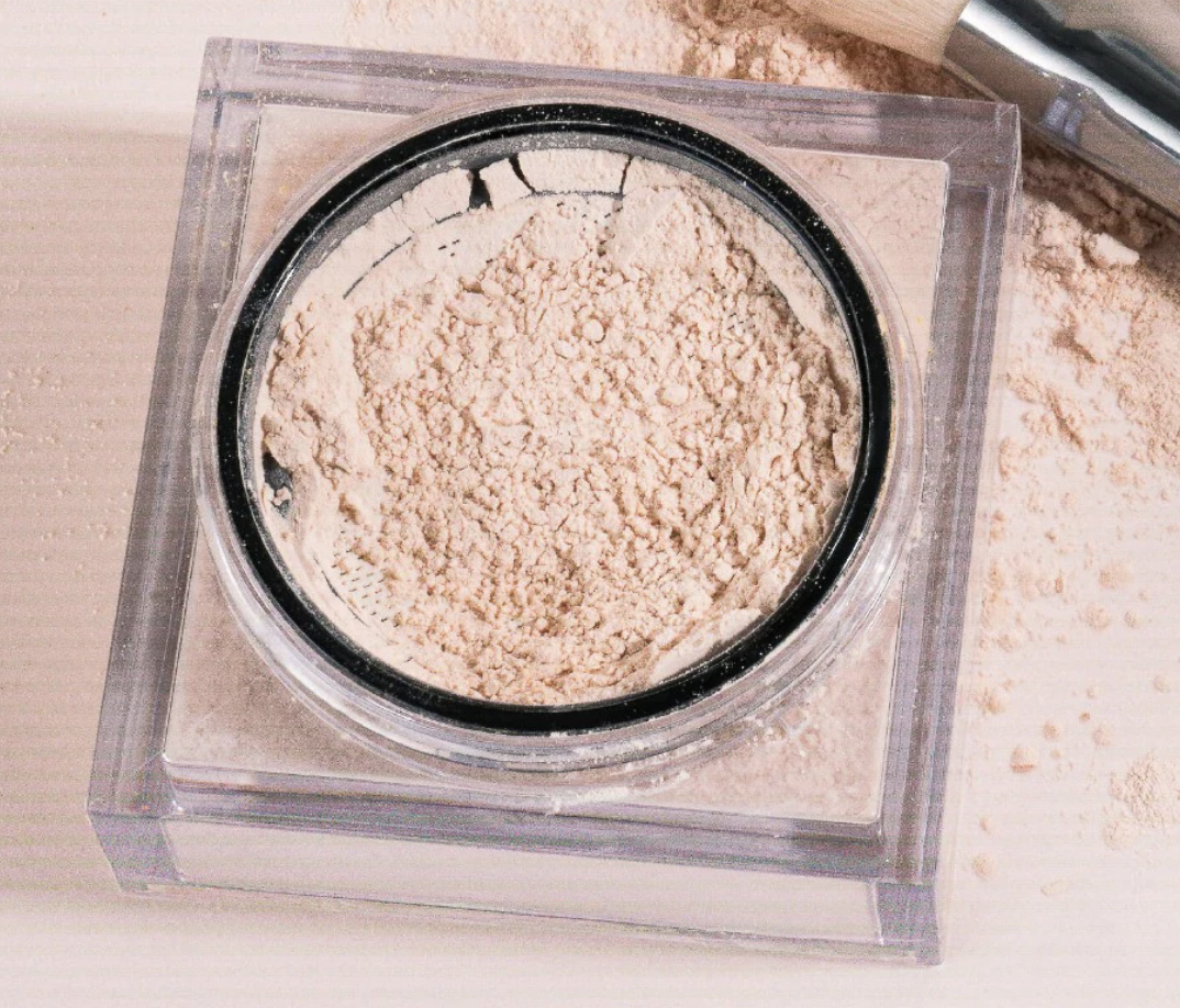 the loose powder open on a table next to a brush