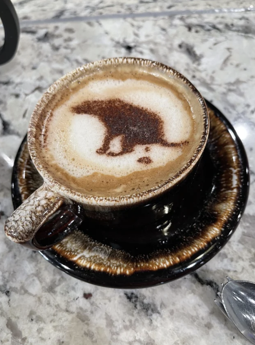 A dog pooping outlined in the foam of a cup of coffee