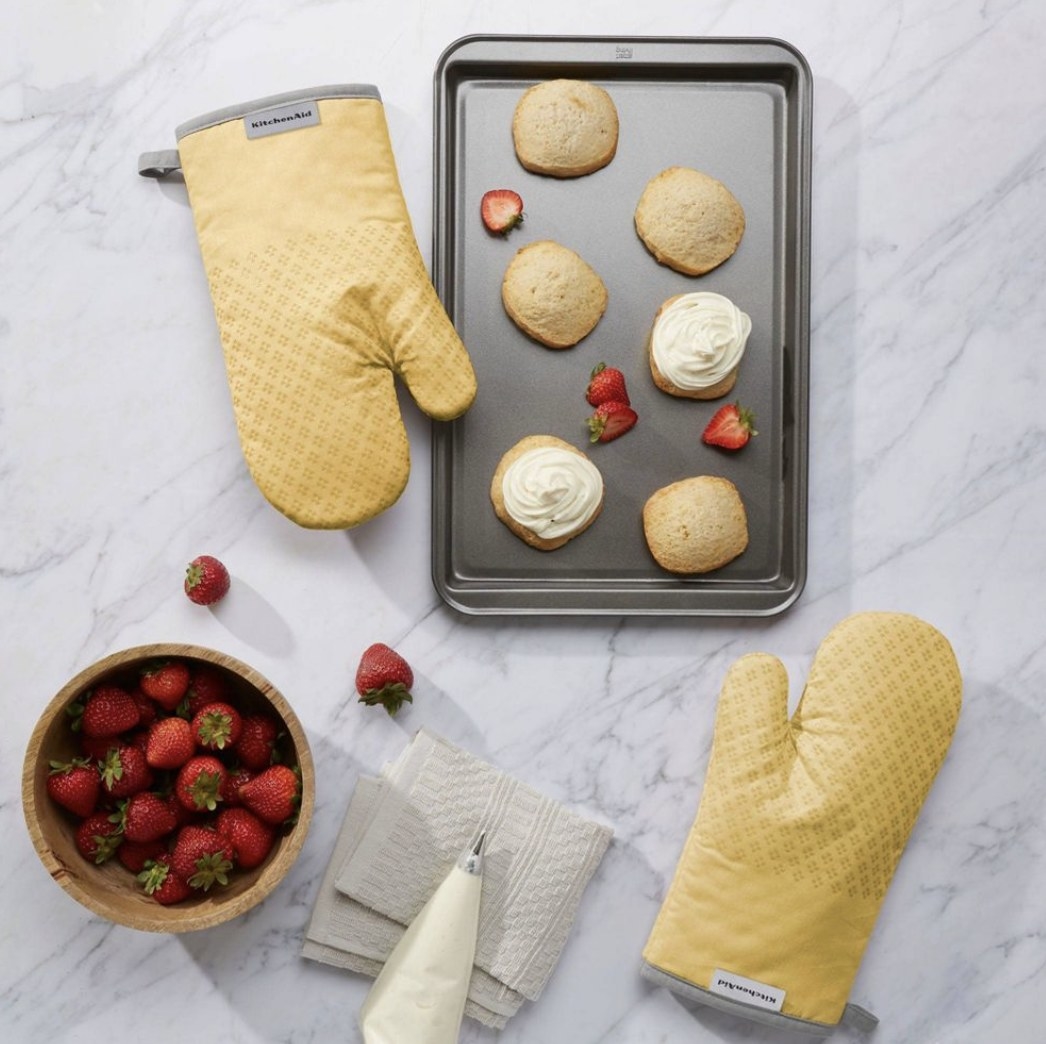 Two yellow oven mitts by a tray of cookies