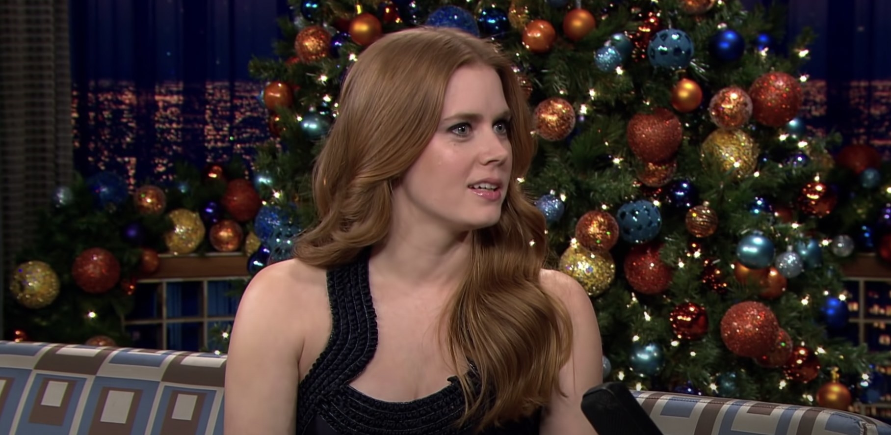 Amy Adams sits on a couch in front of a Christmas tree