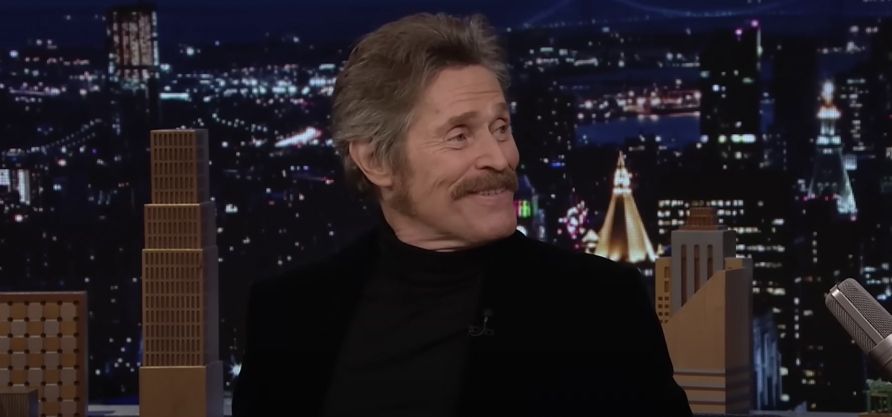 Willem Dafoe raises his eyebrows and smiles
