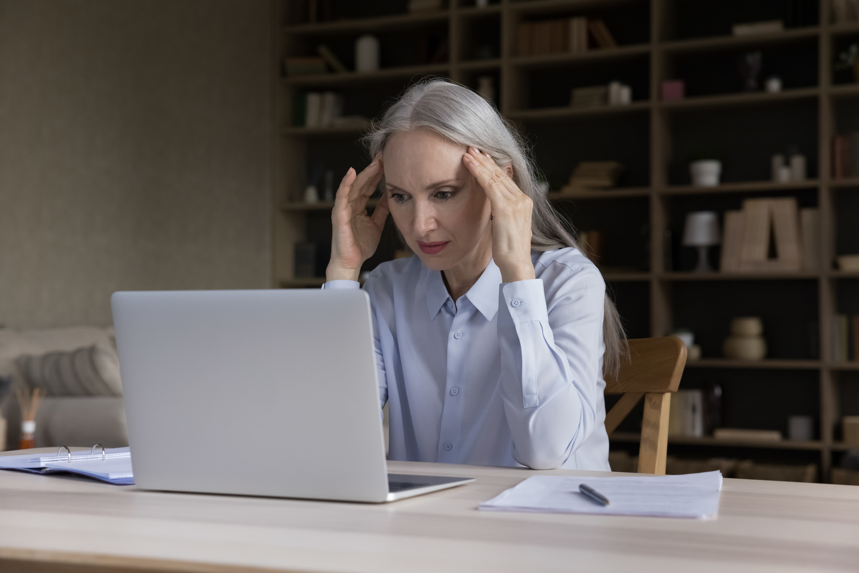 A woman, with her hands on her temples, stares at her computer screen