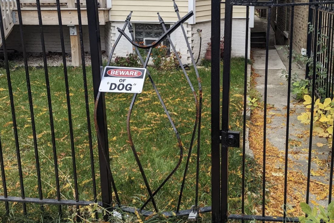 A broken fence with the bars bent, with &quot;Beware of &#x27;dog&#x27;&quot; on it