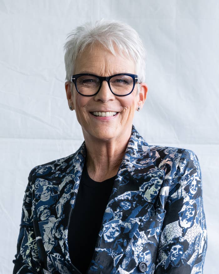 A closeup of Jamie smiling. She&#x27;s wearing a plain top, a patterned jacket, and eyeglasses