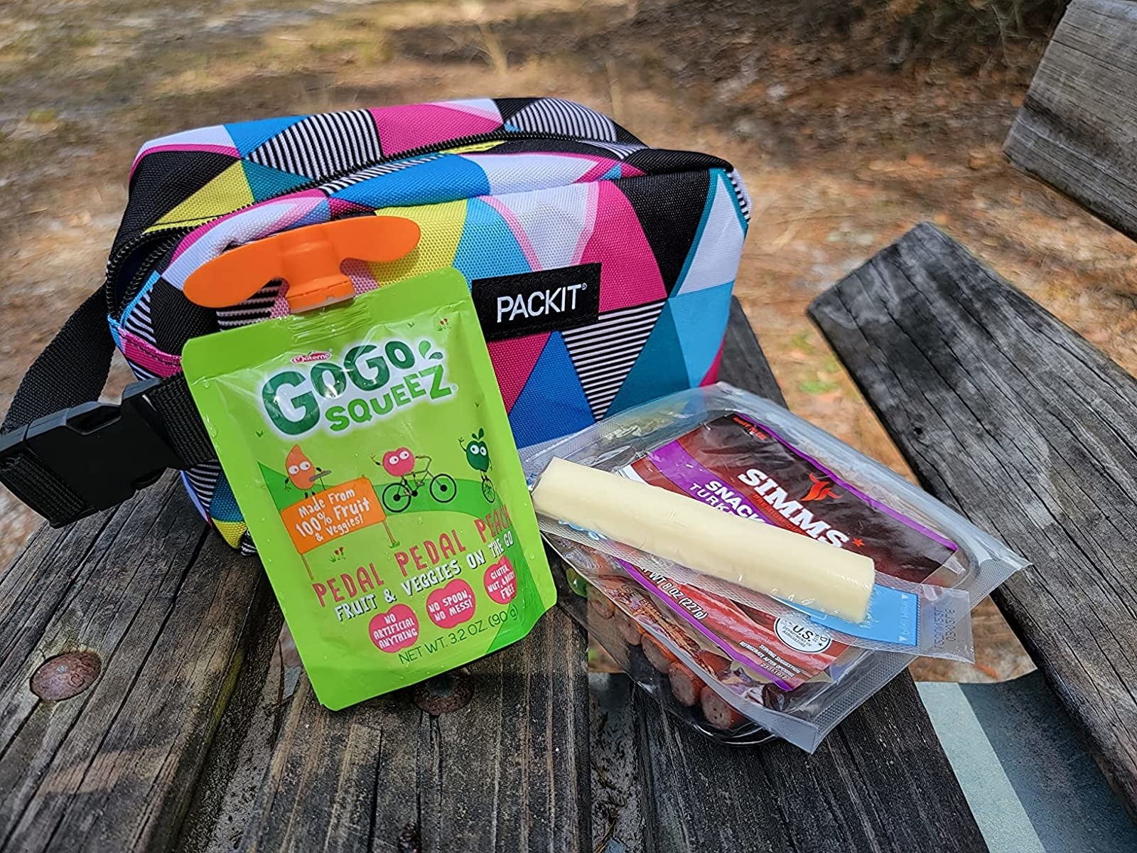 Reviewer&#x27;s photo of the snack box in the color Triangle Stripes posed with a squeezable apple sauce, turkey snacks, and string cheese
