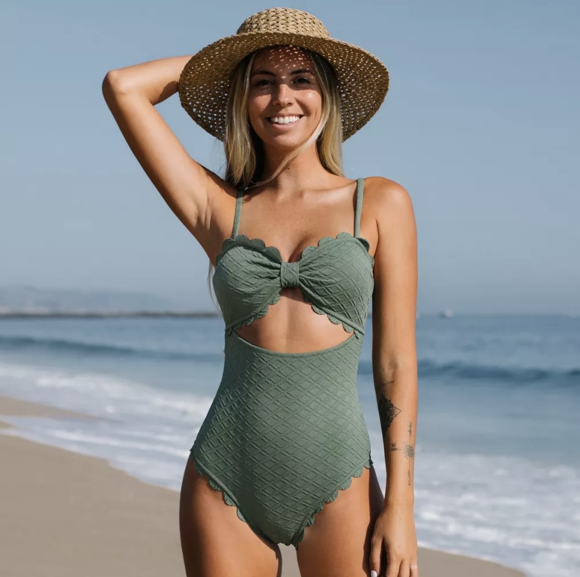 A person wearing a sage green one-piece bathing suit with a cutout in it