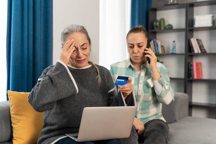 Two women looking sad, one holding a credit card, and one holding a phone
