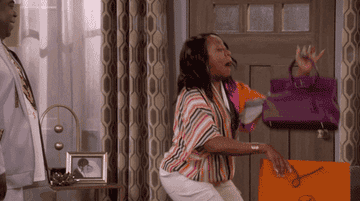 a gif of actor Tichina Arnold in the show &quot;The Neighborhood&quot; pulling a purse out of a shopping bag and screaming in excitement