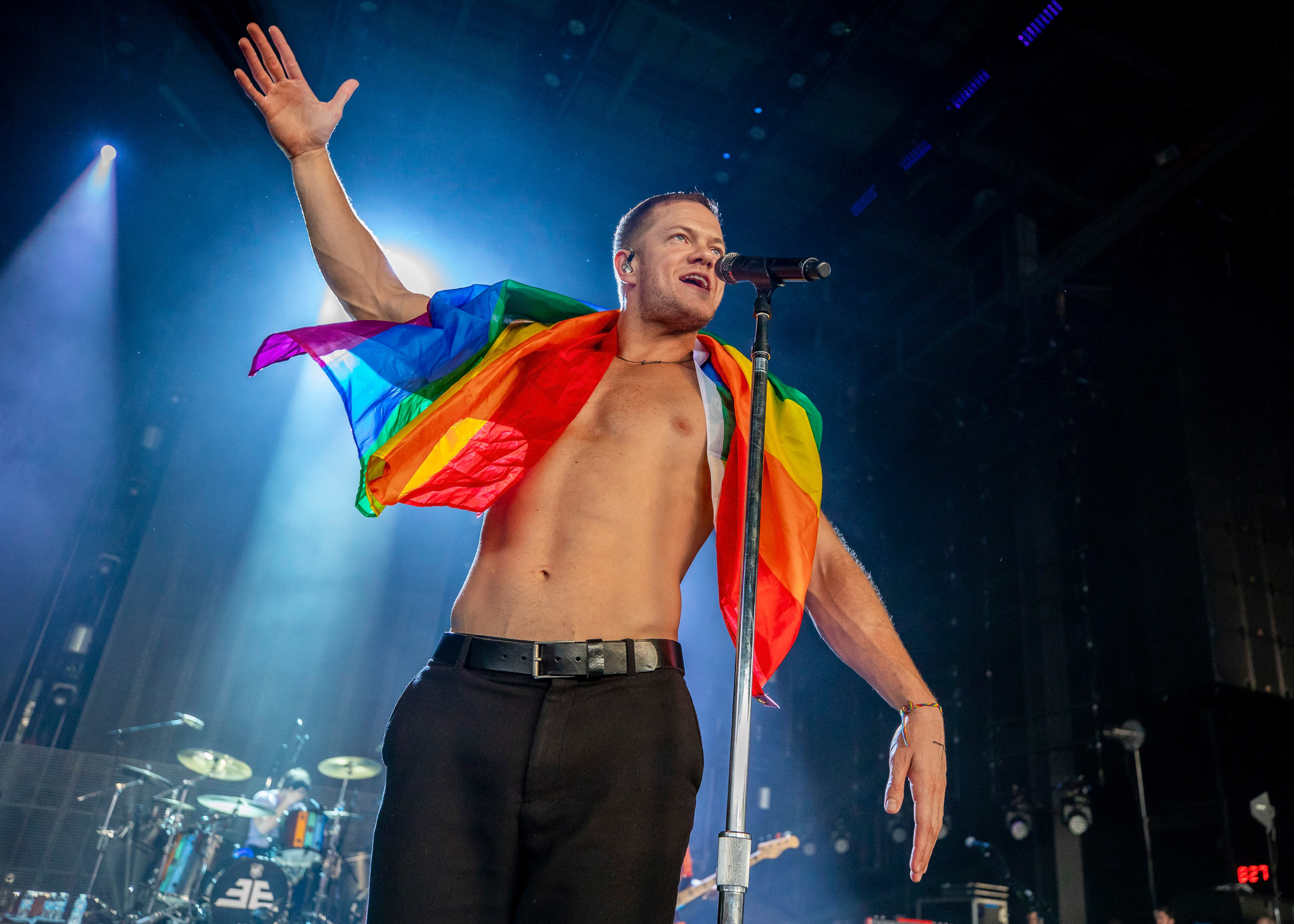 Dan singing shirtless with the Pride flag draped across his shoulders