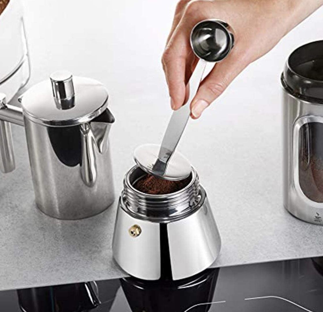 a person using the base of the spoon to tamp coffee in an espresso pot