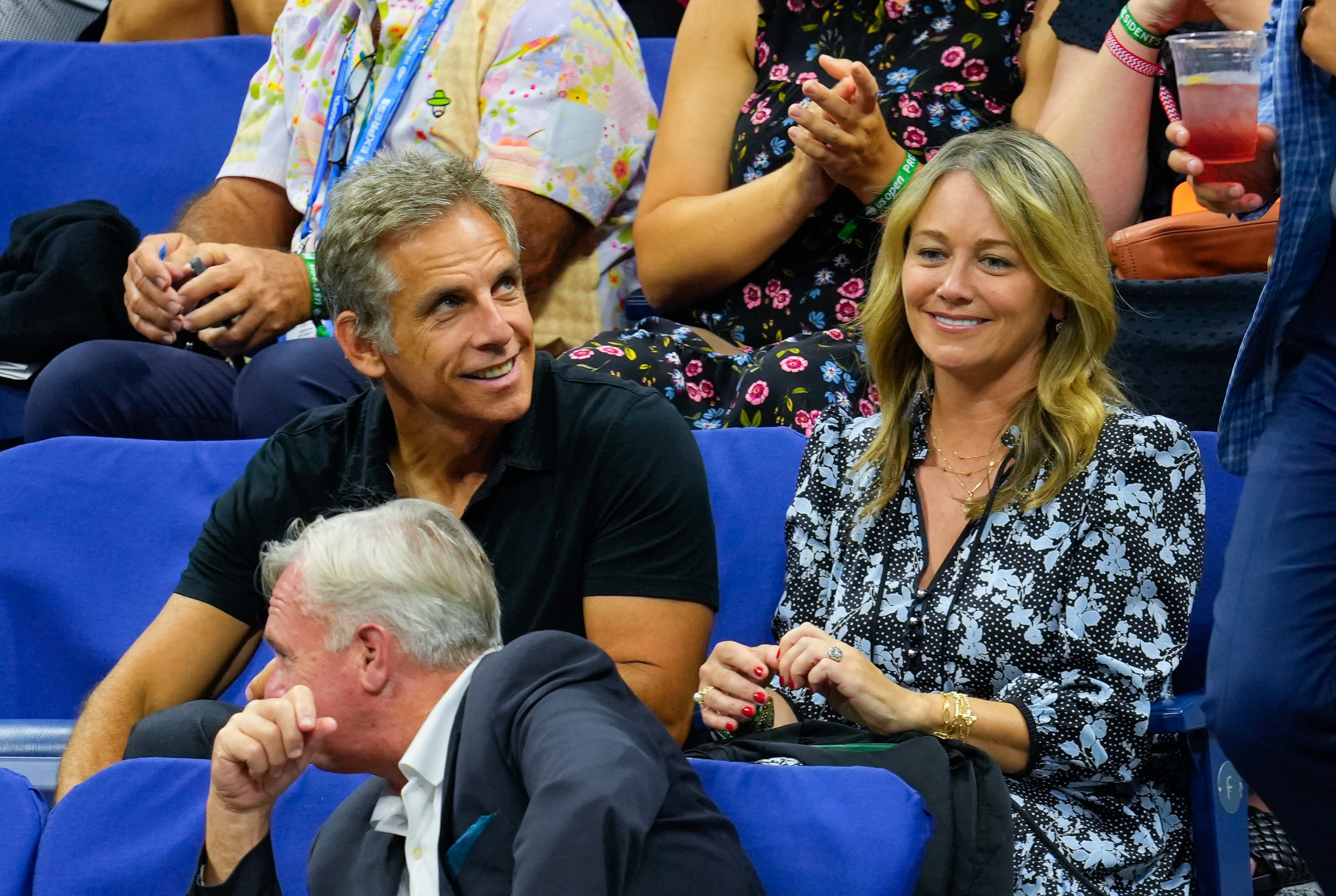 The two smiling as they sit at a sports event