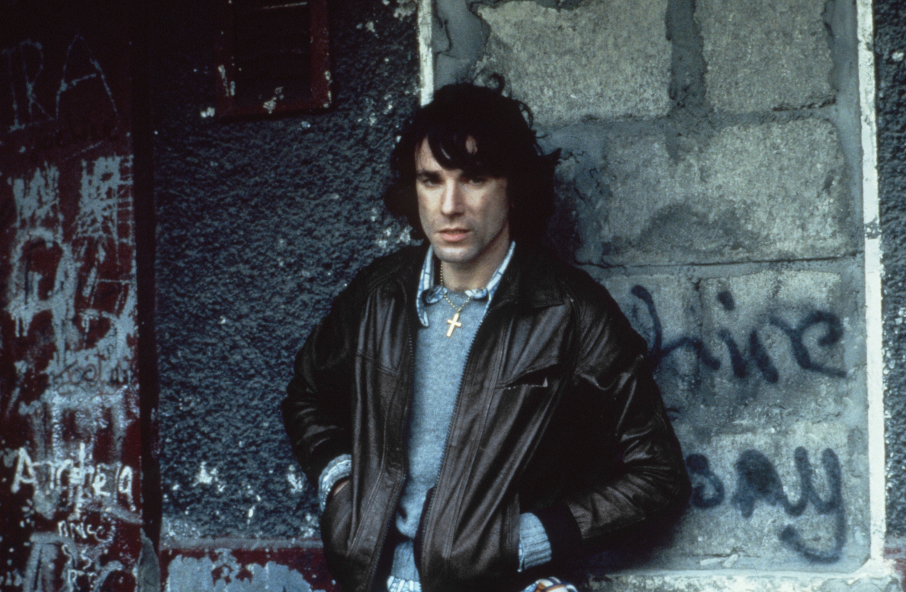 Daniel Day-Lewis leaning against a wall with graffitti