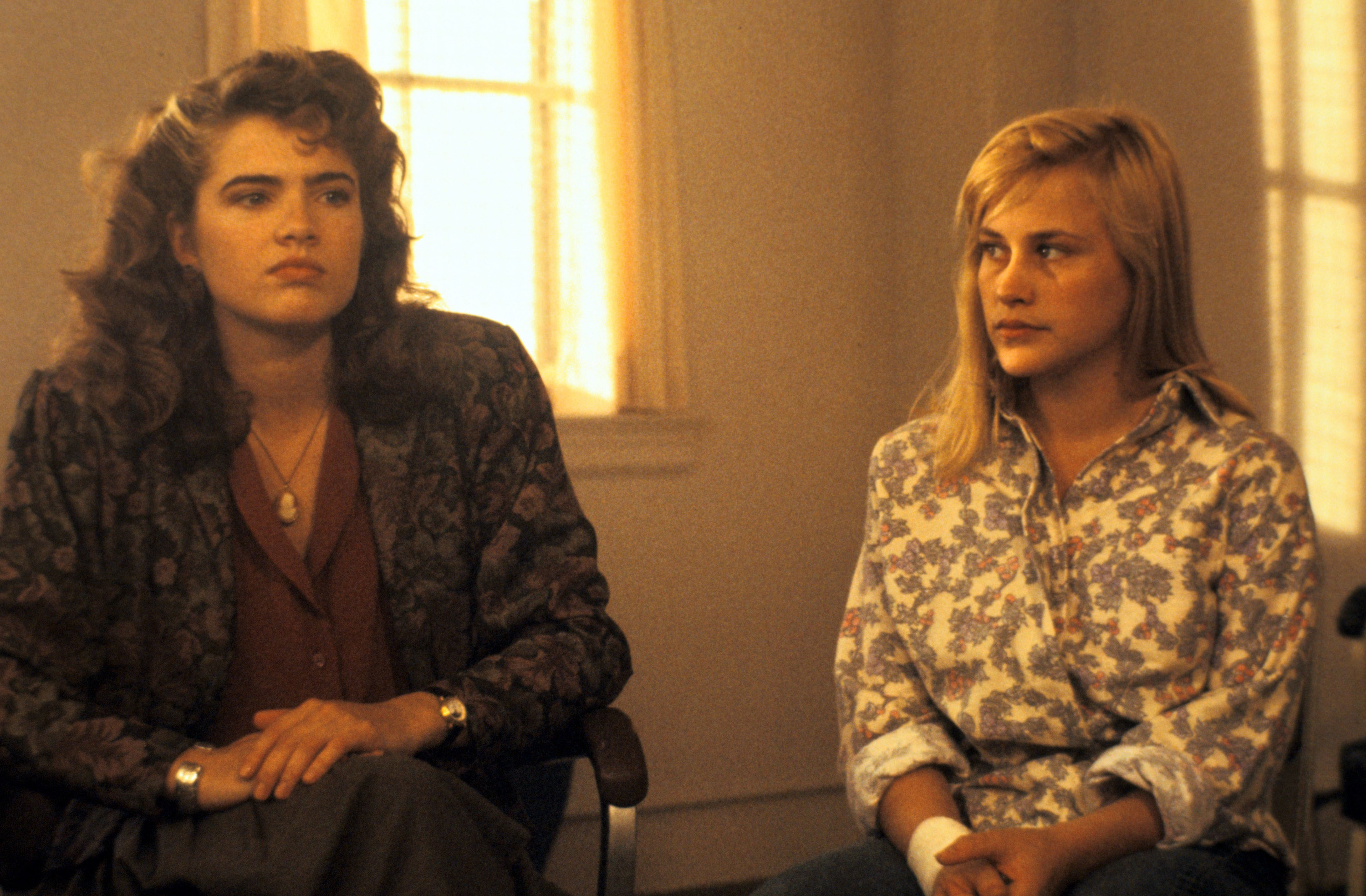 Two young women sit in a group meeting in &#x27;80s floral garb