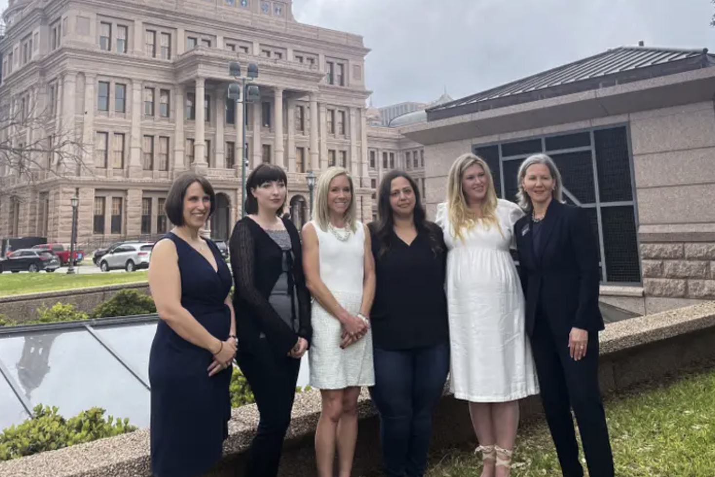 a row of women in black and white formalwear stand in front of the texas capitol