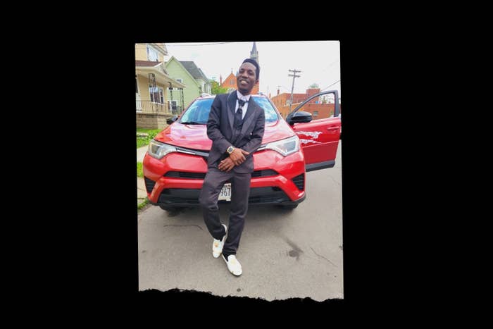 a man in a suit leans against his red car