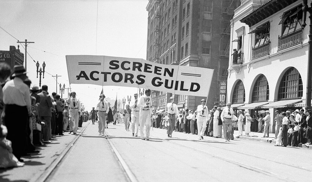 people marching the street with a large sign reading screen actors guild