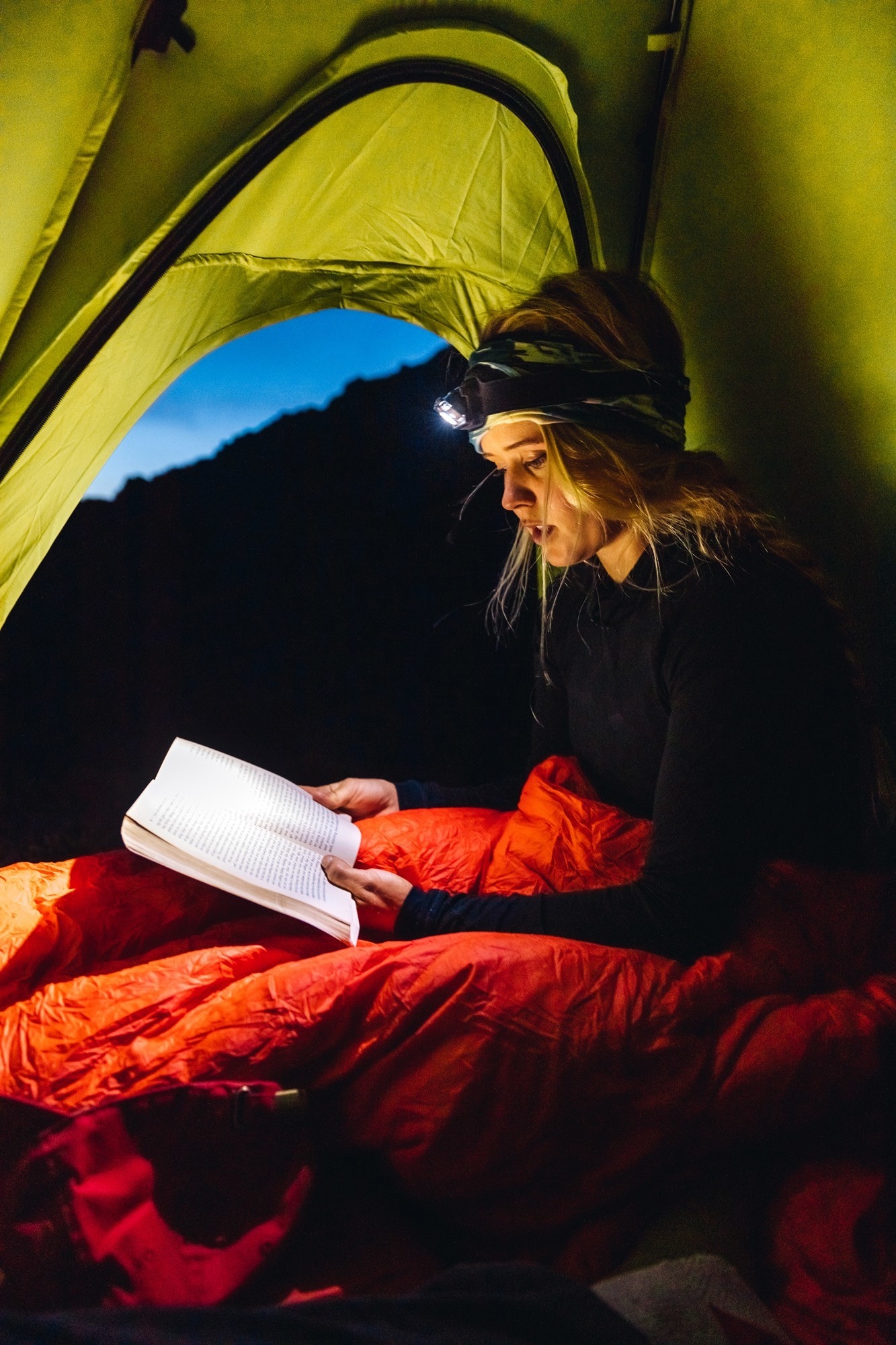 model using the headlamp to read a book in a tent