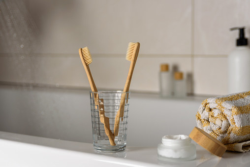 Two bamboo toothbrush in bathroom with towel, body cream and flowing water