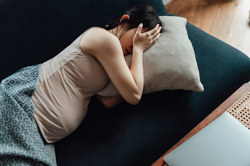 Pregnant woman covering her eyes with hands while laying on sofa