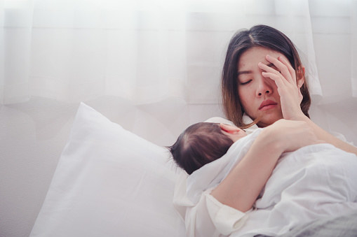 woman holding a baby in bed, while she looks visibly stressed and tired