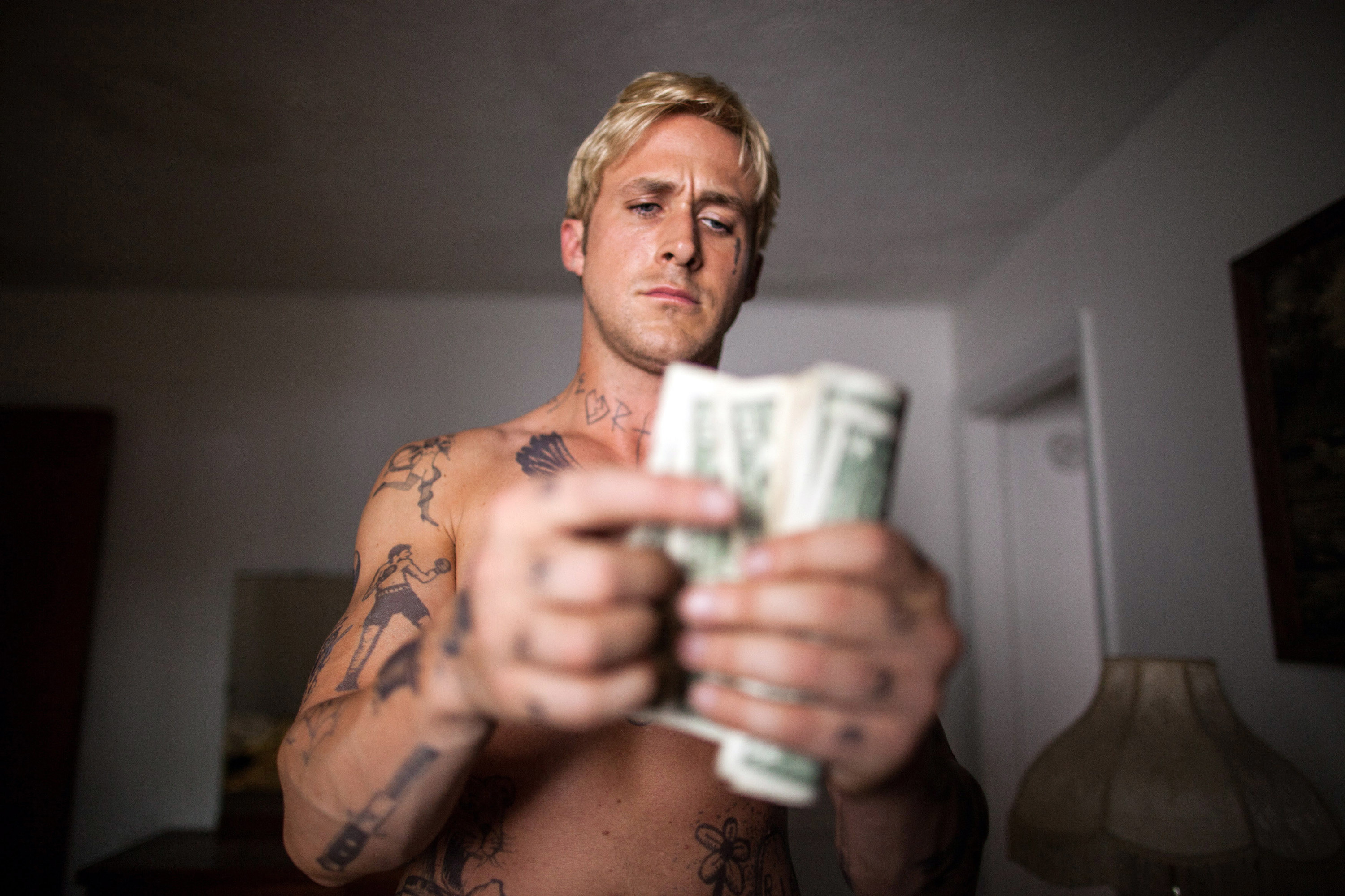 A shirtless tattooed man counts cash