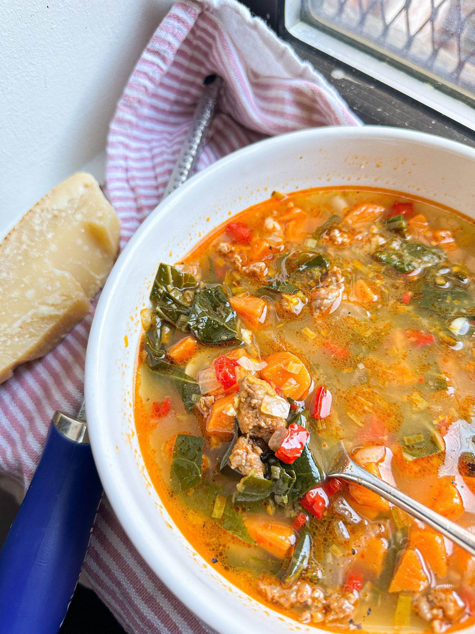 Spoonful of soup in a bowl with greens, sausage, sweet potato, and red pepper