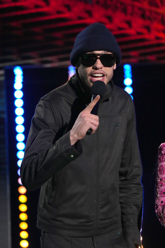 Pete holding a microphone and wearing sunglasses, a beanie, and a jacket
