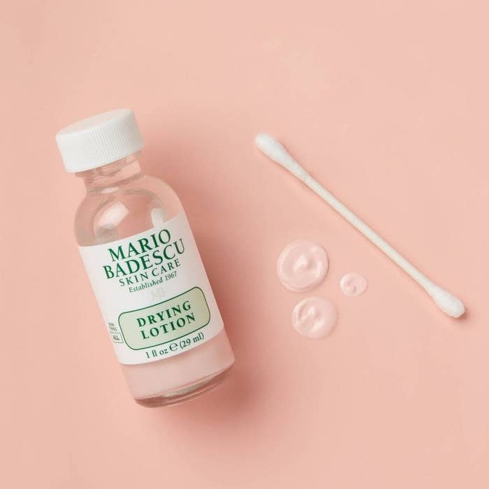 A green and white bottle of acne treatment with a q-tip and product on pink