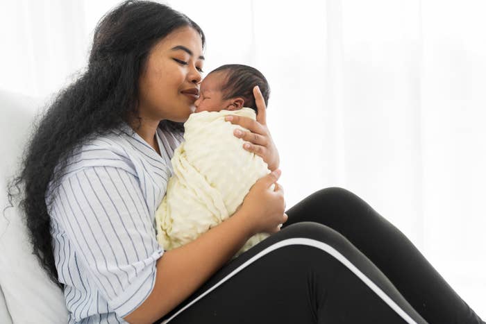 Happy mother carrying and kissing on newborn baby on bed