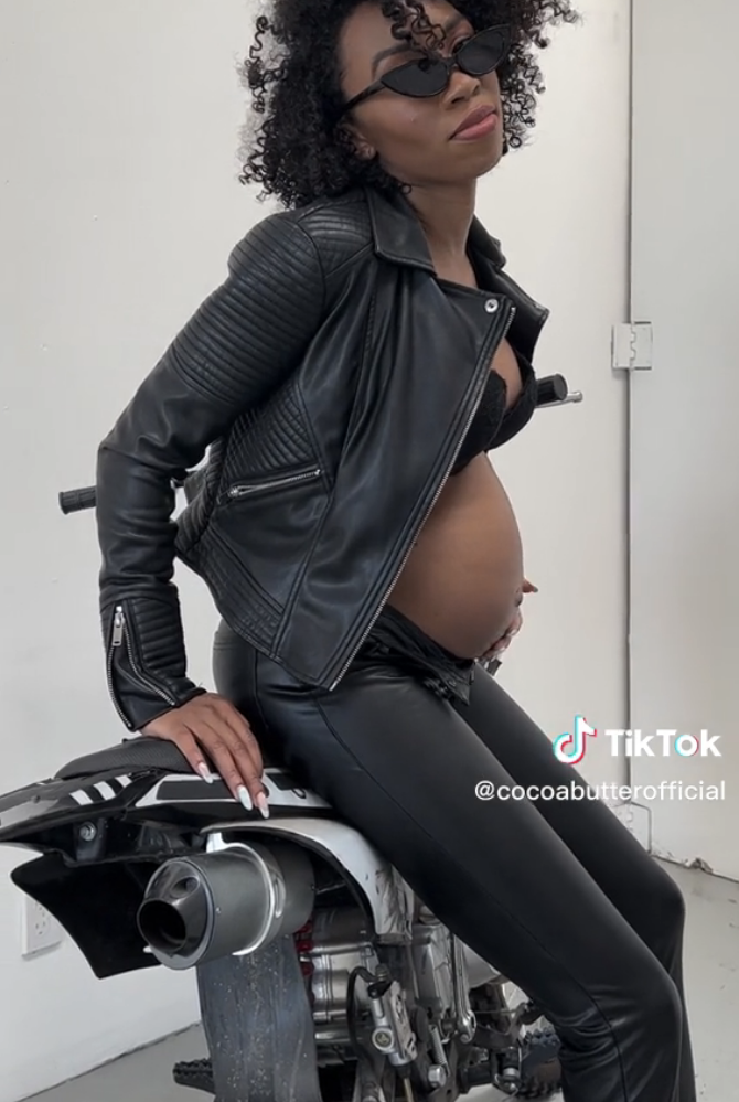 Carrie dressed in a leather jacket and pants, while sitting on a motorcycle, showing off her baby bump
