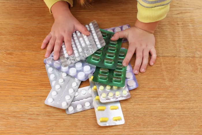 A toddler&#x27;s arms reach for pile of pills in packaging on the table