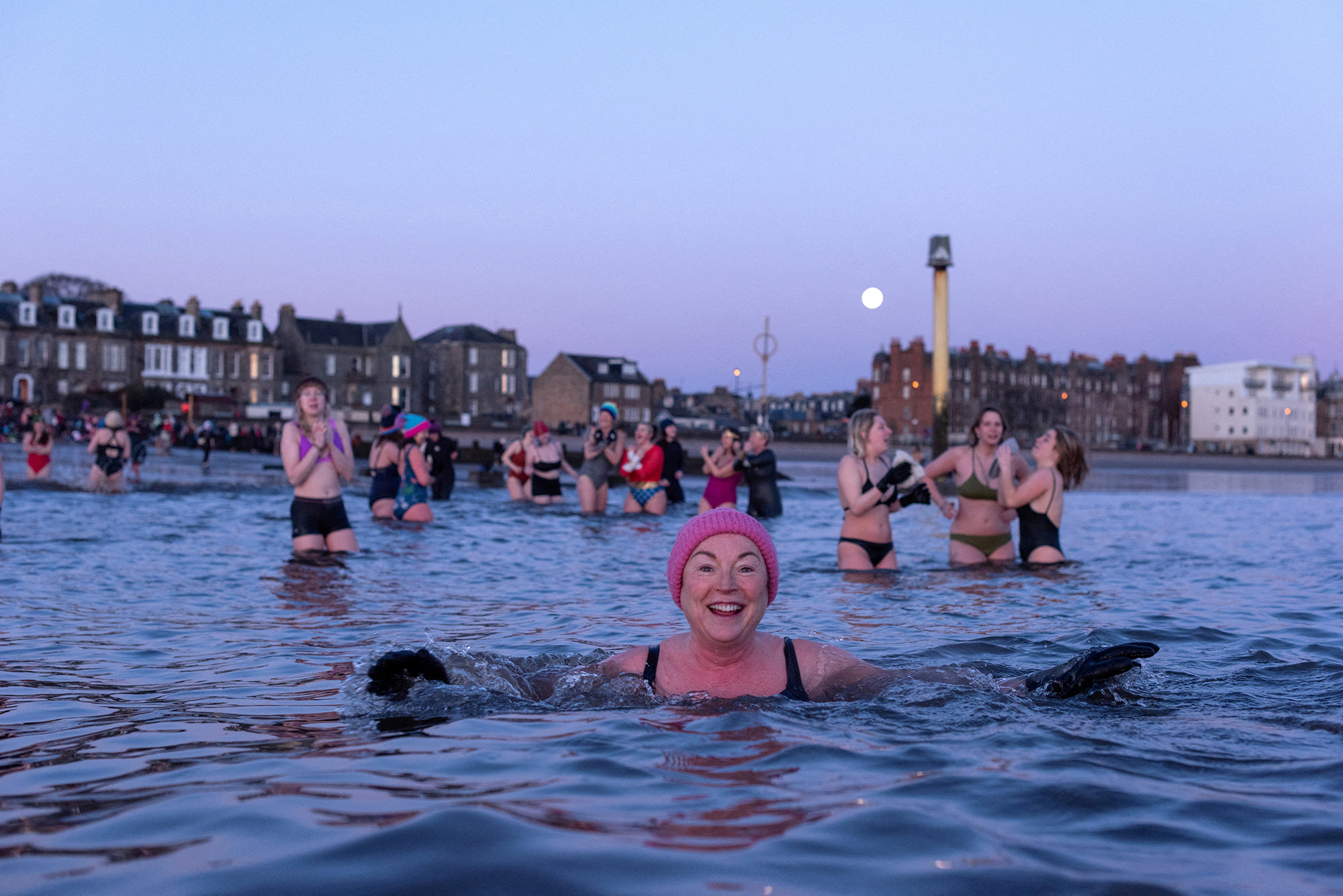 a smiling woman in a pink swim cap treads water in the edinburgh scotland