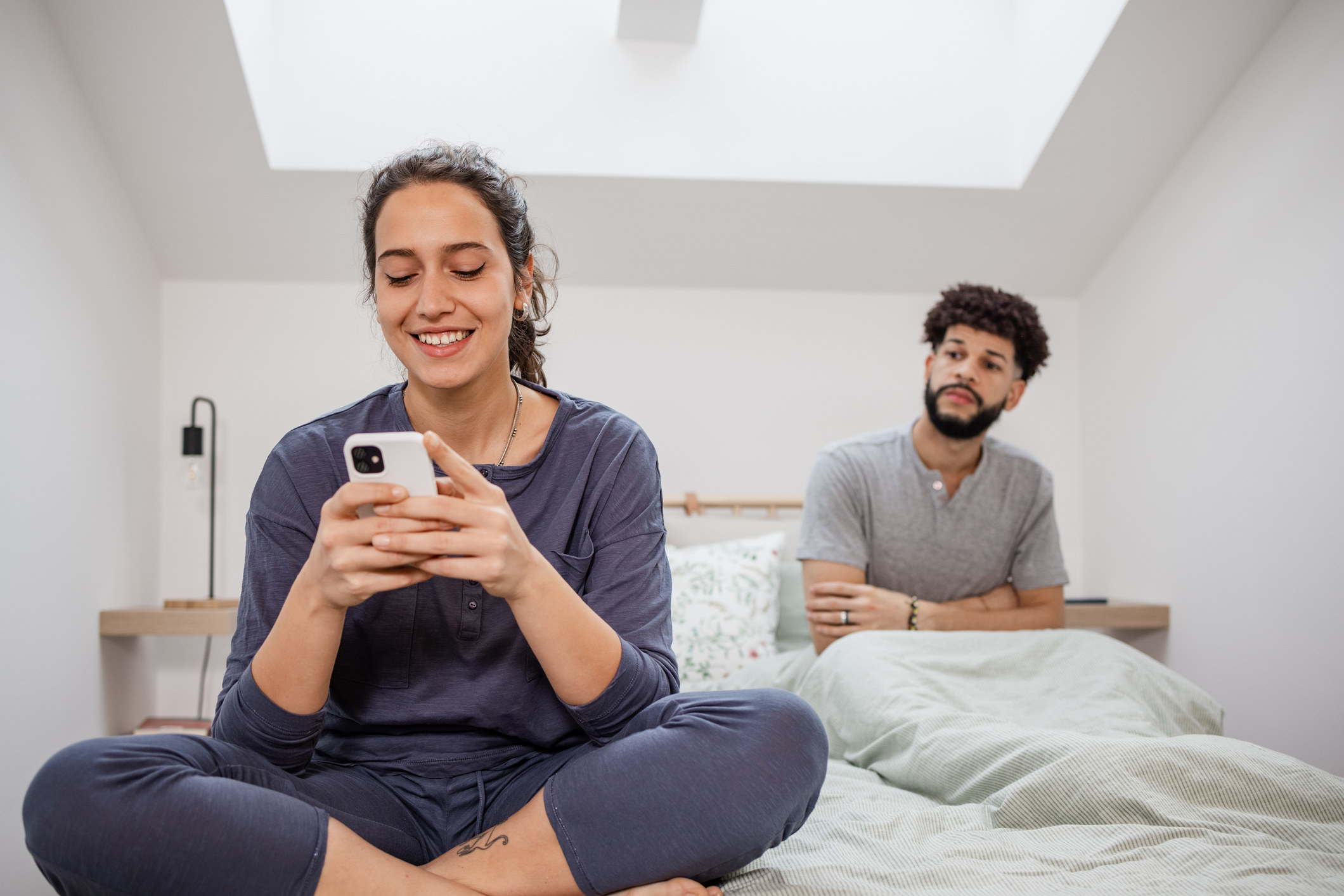 Woman happily texting someone while in bed with a man