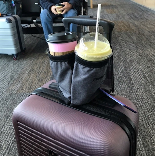 Reviewer&#x27;s photo of the cup holder in the color Carbon Black, strapped to a purple suitcase and holding two drinks