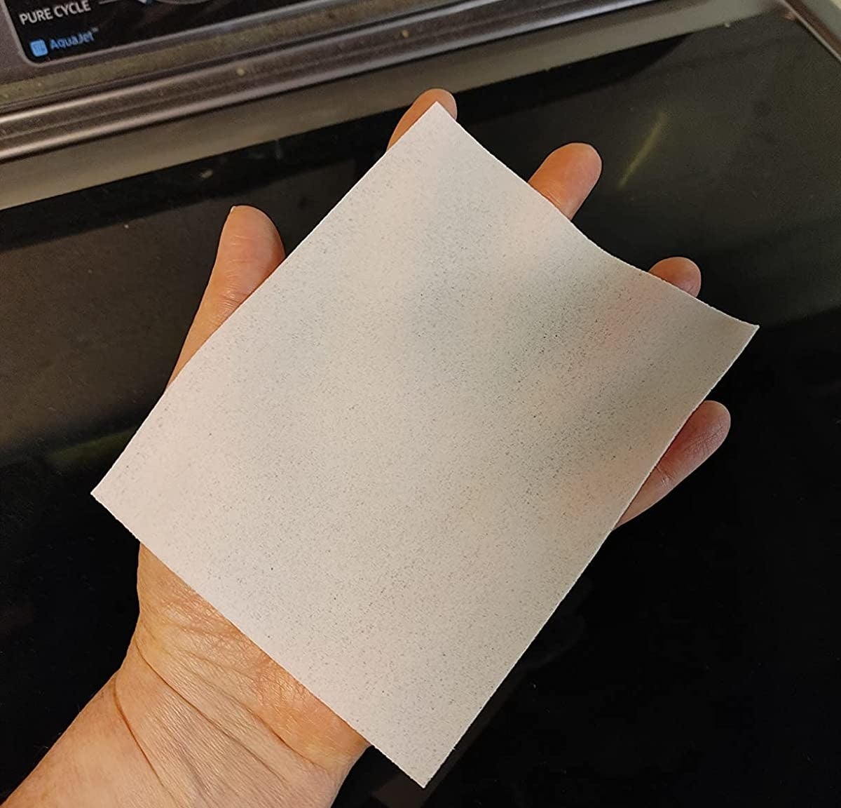 Reviewer&#x27;s photo of a hand holding one of the detergent sheets