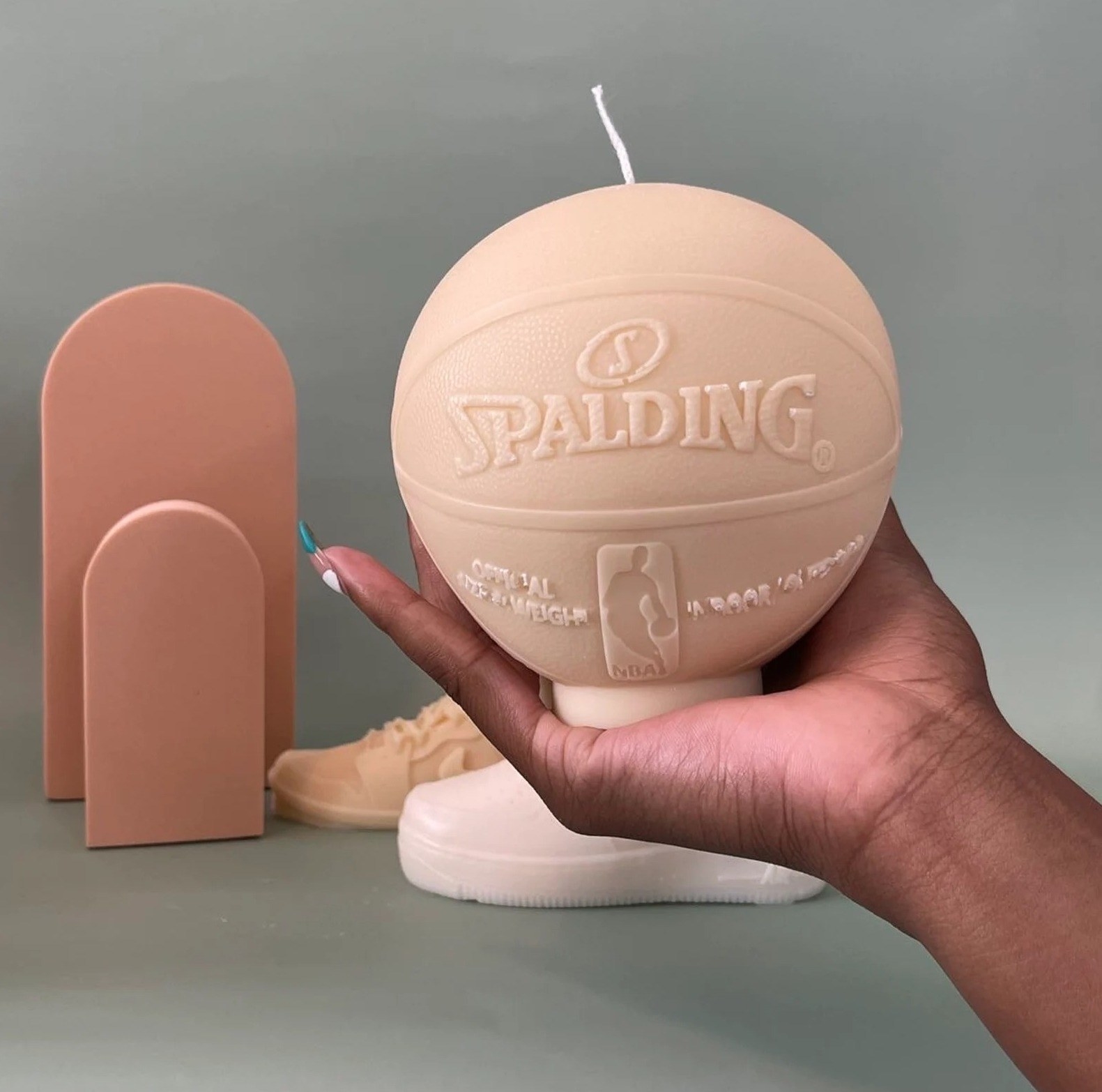 A hand holds a beige candle in the form of a small basketball
