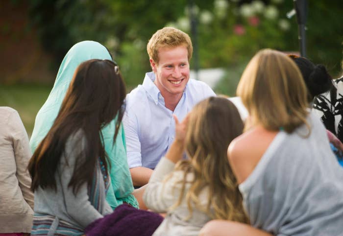 A man who looks like prince harry (but honestly not THAT much like prince harry) surrounded by a group of adoring women