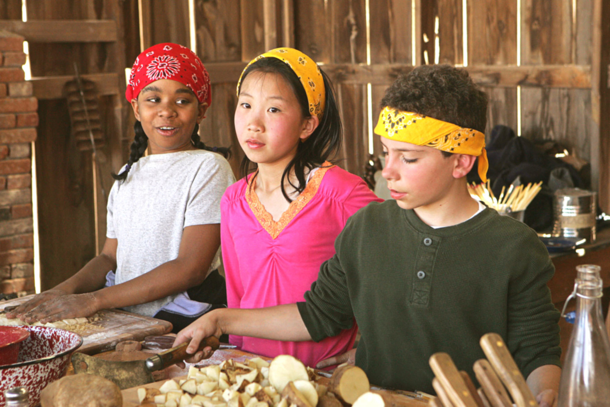 a group of kids in bandanas who look kind of over it cooking a meal in a dilapidated barn