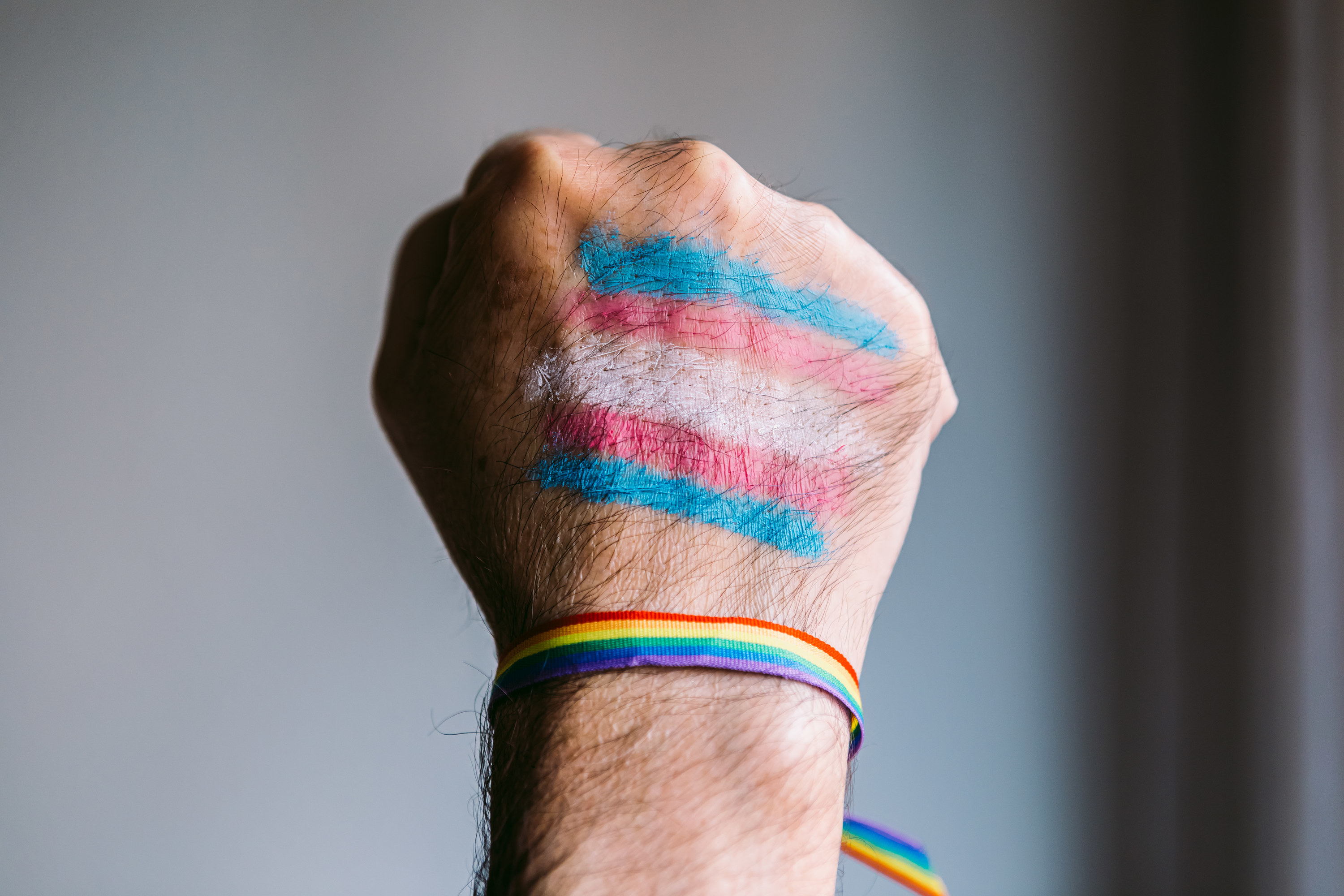 Clenched fist with a painted trans flag and an LGTBIQ flag bracelet