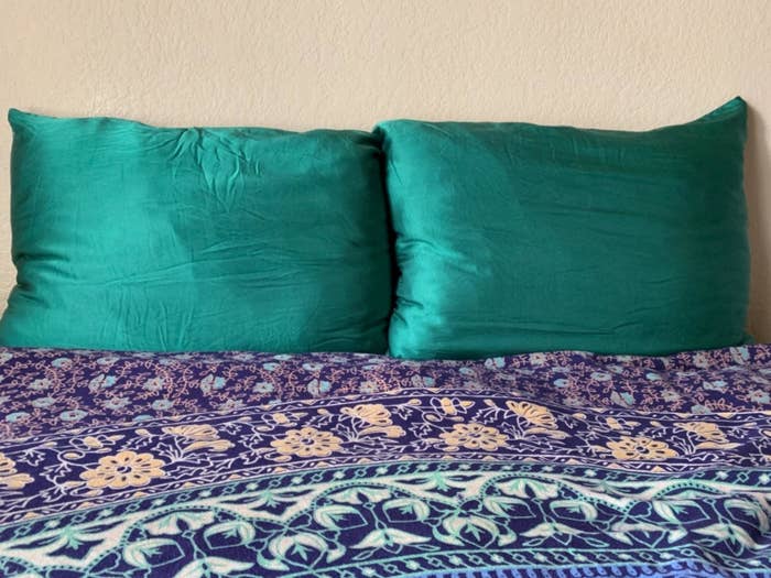 A reviewer&#x27;s photo of the emerald green pillowcases covering pillows on a bed