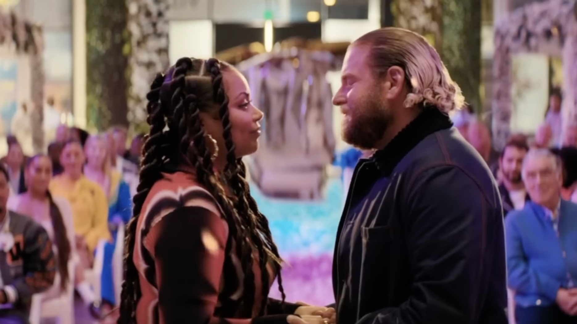 Jonah Hill and Lauren London stand at an altar, with people sitting on chairs watching them