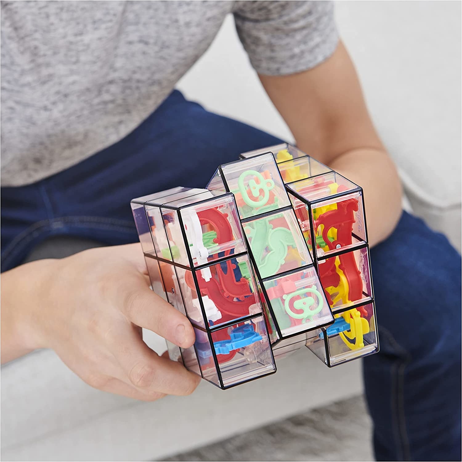 Model&#x27;s hands playing with clear Rubik&#x27;s Cube-like toy with colorful mazes inside