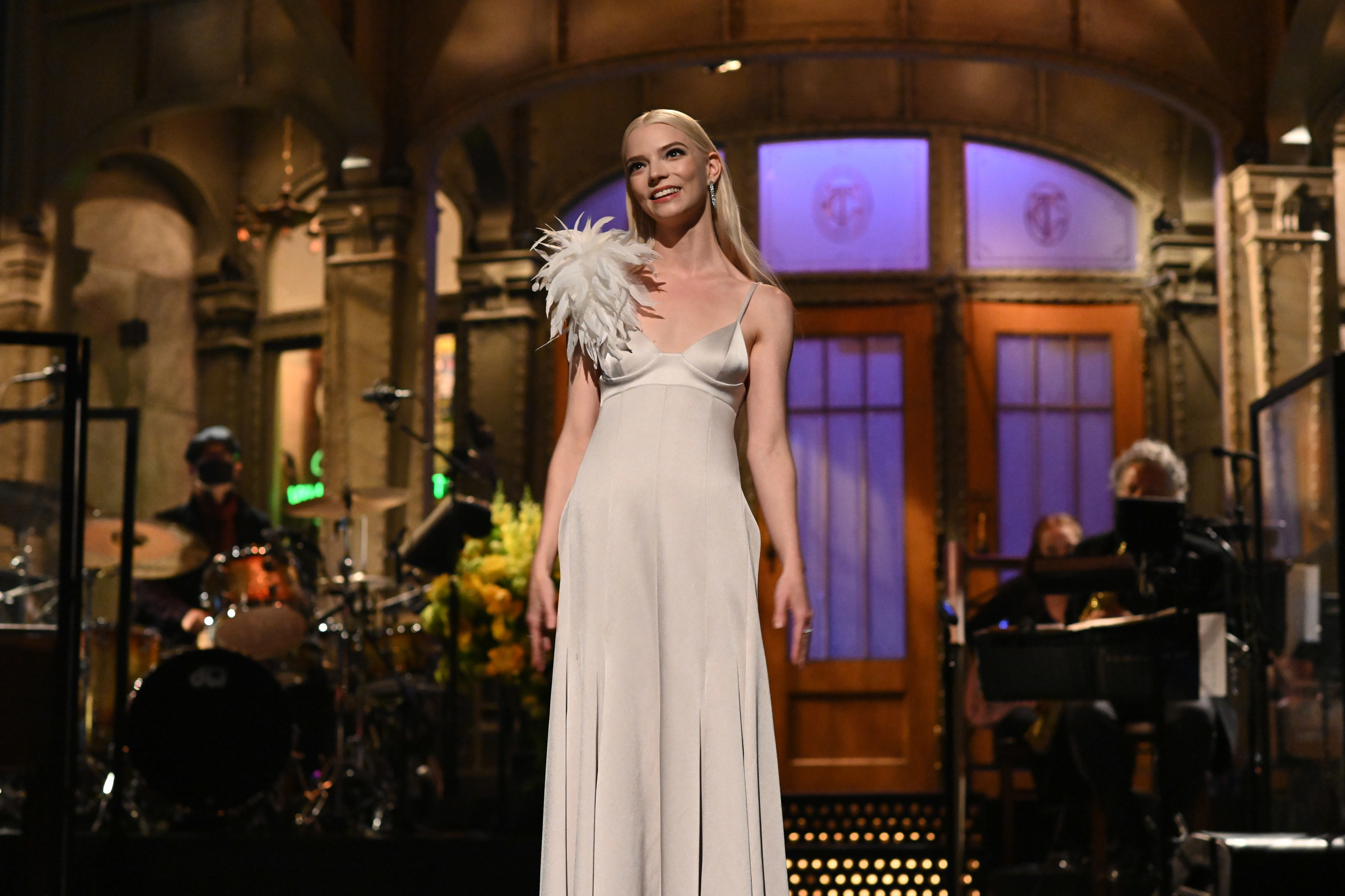 Anya delivering her SNL monologue while wearing a satin dress with feathers on one shoulder