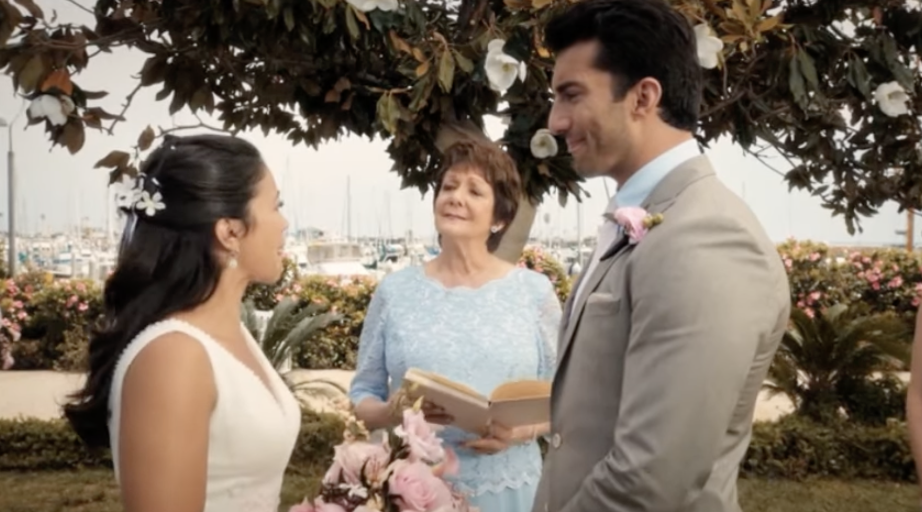 Jane, in a wedding dress, stands opposite Rafael, in a gray suit, while her grandmother stands between them reading from a book
