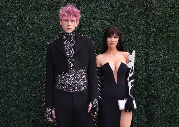 The couple holding hands as they stand in front a grass wall as they pose for photos at an event